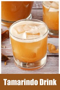 two glasses filled with orange juice and ice sitting on top of a wooden table next to an