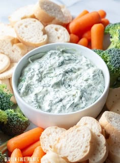 a bowl of dip surrounded by carrots, broccoli and crackers