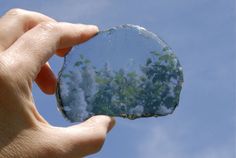 a hand holding a piece of glass in the air with clouds and blue sky behind it