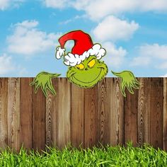 the grin face is peeking out from behind a wooden fence with green grass and blue sky in the background