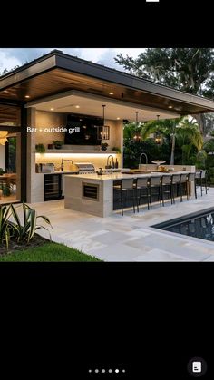 an outdoor kitchen next to a swimming pool with bar stools on the side and lights hanging from the ceiling