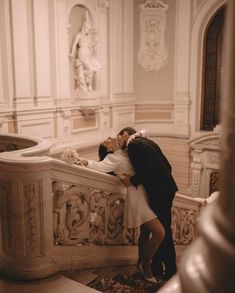 a man and woman are kissing on the stairs in an ornate room with white walls