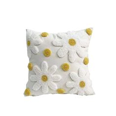 a white pillow with yellow and white flowers on the front, sitting against a white background