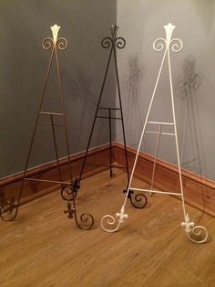 three metal easels sitting on top of a hard wood floor next to a wall