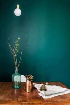 a wooden table topped with a green vase filled with flowers next to a light bulb