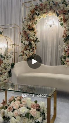 a white couch sitting next to a glass table with flowers on it and a gold frame