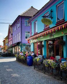 colorful buildings line the side of a cobblestone street with people sitting at tables