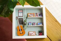 a miniature guitar and other items in a white box on a wooden table next to a potted plant