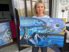 a woman holding up a painting in front of a window with two fish on it