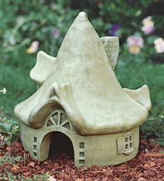 a small clay house sitting in the middle of some grass and dirt with flowers around it