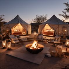 an outdoor fire pit surrounded by chairs and lights in the desert at night with tents set up behind it