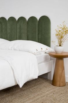 a white bed sitting next to a green headboard on top of a wooden table