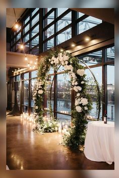 a wedding arch decorated with flowers and candles in front of a window overlooking the water