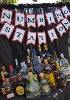 there are many liquor bottles on the table with bunting signs above them that read, numbing station