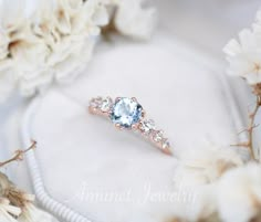 an engagement ring with blue topaz sits on a white cloth surrounded by flower petals