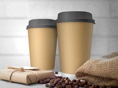 two coffee cups sitting on top of a table next to some beans and a bag