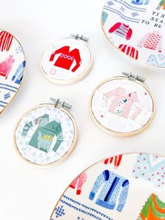 four embroidery hoop frames with different designs on them and one has an ornament in the shape of a house