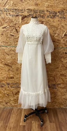 a white dress on a mannequin stand in front of a wooden wall