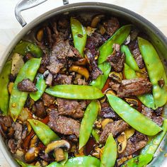 a pan filled with meat and vegetables on top of a wooden table next to a knife