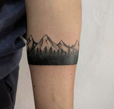 a tattoo on the arm of a person with mountains in the background and trees behind it