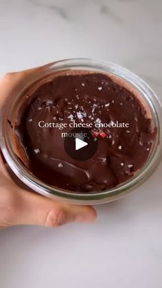 a person holding a glass jar filled with chocolate cake in it's left hand