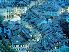 many buildings are lit up at night in an old european city with steeple roofs