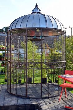 a gazebo sitting on top of a wooden deck next to a red table and chairs