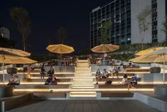 several people sitting on steps with umbrellas over them in front of a building at night