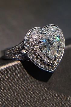 a heart shaped diamond ring sitting on top of a piece of cloth next to a window