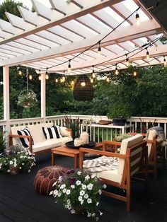 an outdoor patio with white furniture and string lights hanging from the pergolated roof