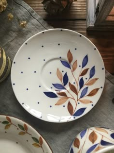 three plates with leaves painted on them sitting on top of a table next to other dishes