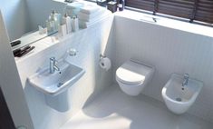 a white bathroom with two toilets and a sink