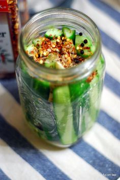 a jar filled with cucumbers and spices on top of a striped table cloth