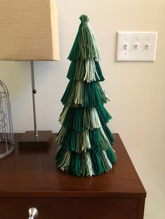 a christmas tree made out of yarn sitting on top of a dresser next to a lamp