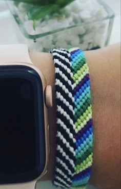 an apple watch on someone's arm with a colorful bracelet around the wrist and a flower pot in the background