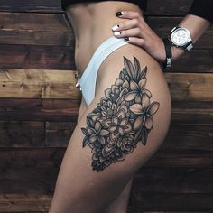 a close up of a person's thigh with flowers tattooed on the leg and behind her is a wooden wall