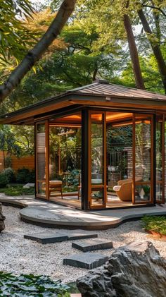 a gazebo in the middle of a garden surrounded by rocks and trees with chairs around it