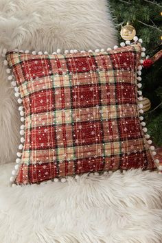 a red plaid pillow sitting on top of a wooden chair next to a christmas tree