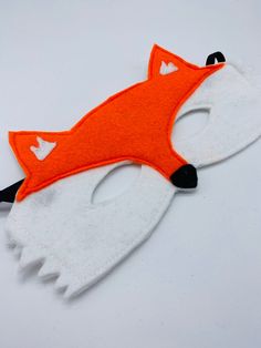 an orange and white felt fox mask on a white surface with black eyeliners