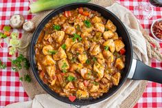 a skillet filled with chicken and vegetables on top of a checkered table cloth