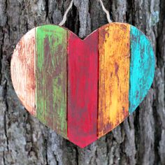 a wooden heart hanging on a tree with the colors of the rainbow painted on it