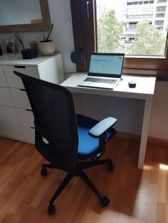 a laptop computer sitting on top of a desk next to a blue chair in front of a window