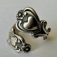 a sweet ring made by Avon, a sturdy wrap ring made in the style of spoon rings.  this is sterling and adorned with hearts and flowers and pretty scrollwork.  it's marked Avon and sterling.  it has light wear, mostly on the inner band, and patina, and is adjustable. size:  7, adjustable height of face:  7/8" width of inner band:  a bit under 1/8" Vintage Sterling Silver Heart Ring, Vintage Sterling Silver Heart Ring Gift, Vintage Heart-shaped Metal Jewelry, Adjustable Heart-shaped Metal Ring, Silver Vintage Heart Bracelet, Adjustable Fit, Sterling Silver Spoon Ring, Sweet Ring, Hearts And Flowers, Sterling Silver Spoons