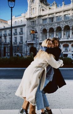 two women hugging each other on the sidewalk in front of a large building with many windows