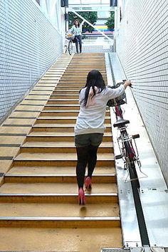 a woman walking down some stairs with her bike on the handle bars and red shoes