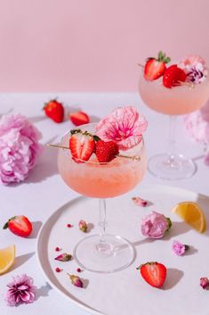 two cocktails with strawberries and flowers on a plate next to pink peonies