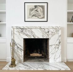 a fireplace in a living room with white walls and marble surround it is surrounded by bookshelves