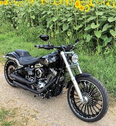 a black motorcycle parked on top of a dirt road next to a field of sunflowers