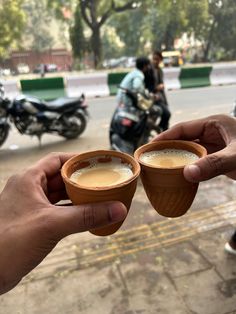 two people holding cups of coffee in their hands on the street with motorcycles behind them