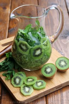 a pitcher filled with kiwi slices on top of a cutting board next to sliced green leaves